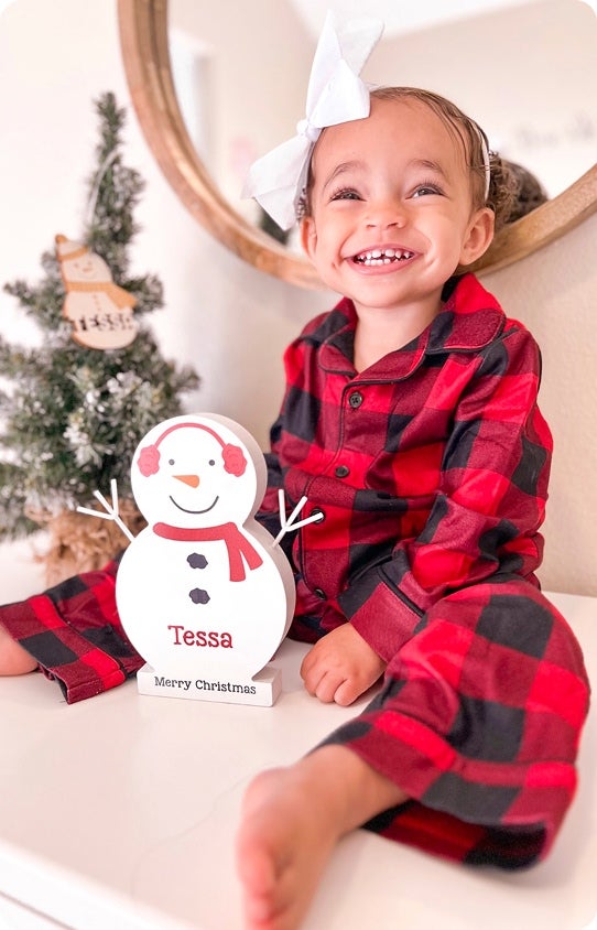 A toddler smiling with a personalized Christmas decor item sitting on a mantel