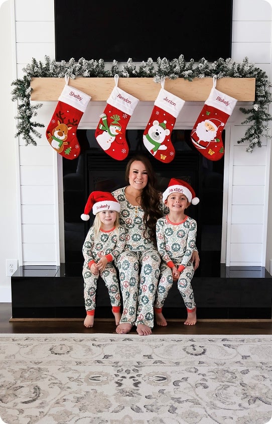 A happy family sitting by the fireplace in matching Christmas pajamas with personalized stockings hung up behind them