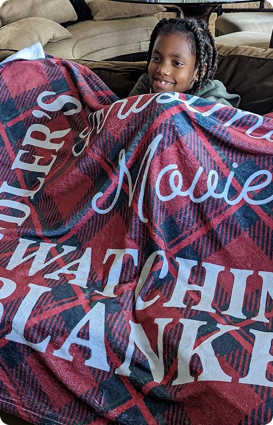 A child happily smiling under a personalized family Christmas blanket