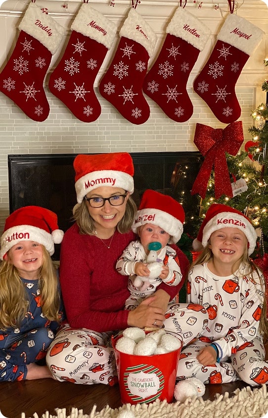 A happy family sitting by the fireplace wearing personalized Santa hats