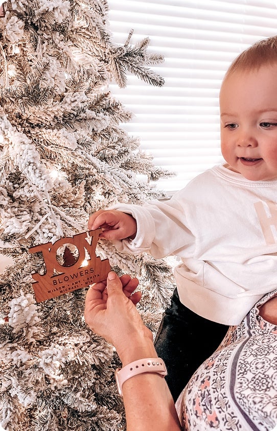 A baby being held in front of a Christmas tree enjoying a personalized Christmas ornament