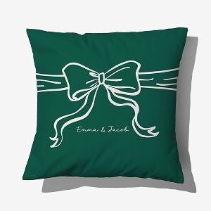 A green personalized pillow with a bow and the names, Emma & Jacob, written on it