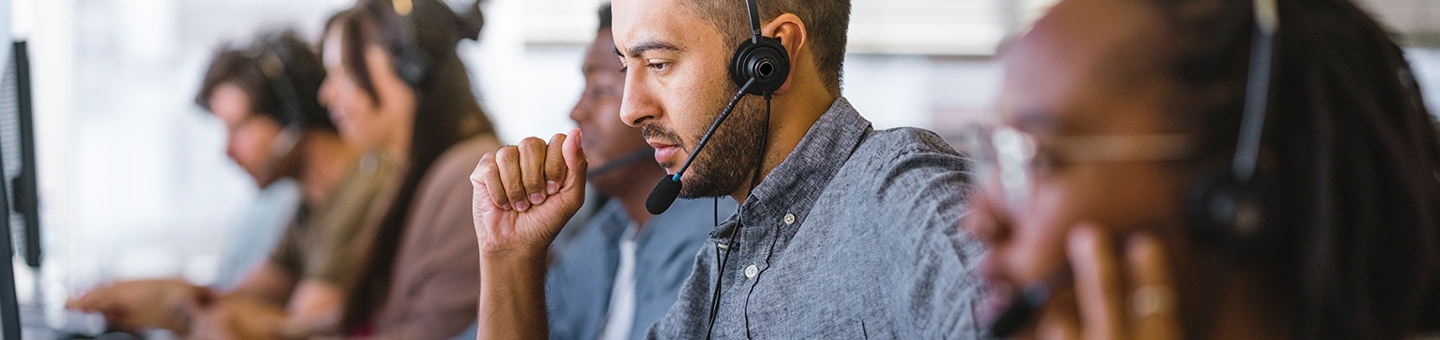 Customer service representatives wearing headsets sit at computers in an office